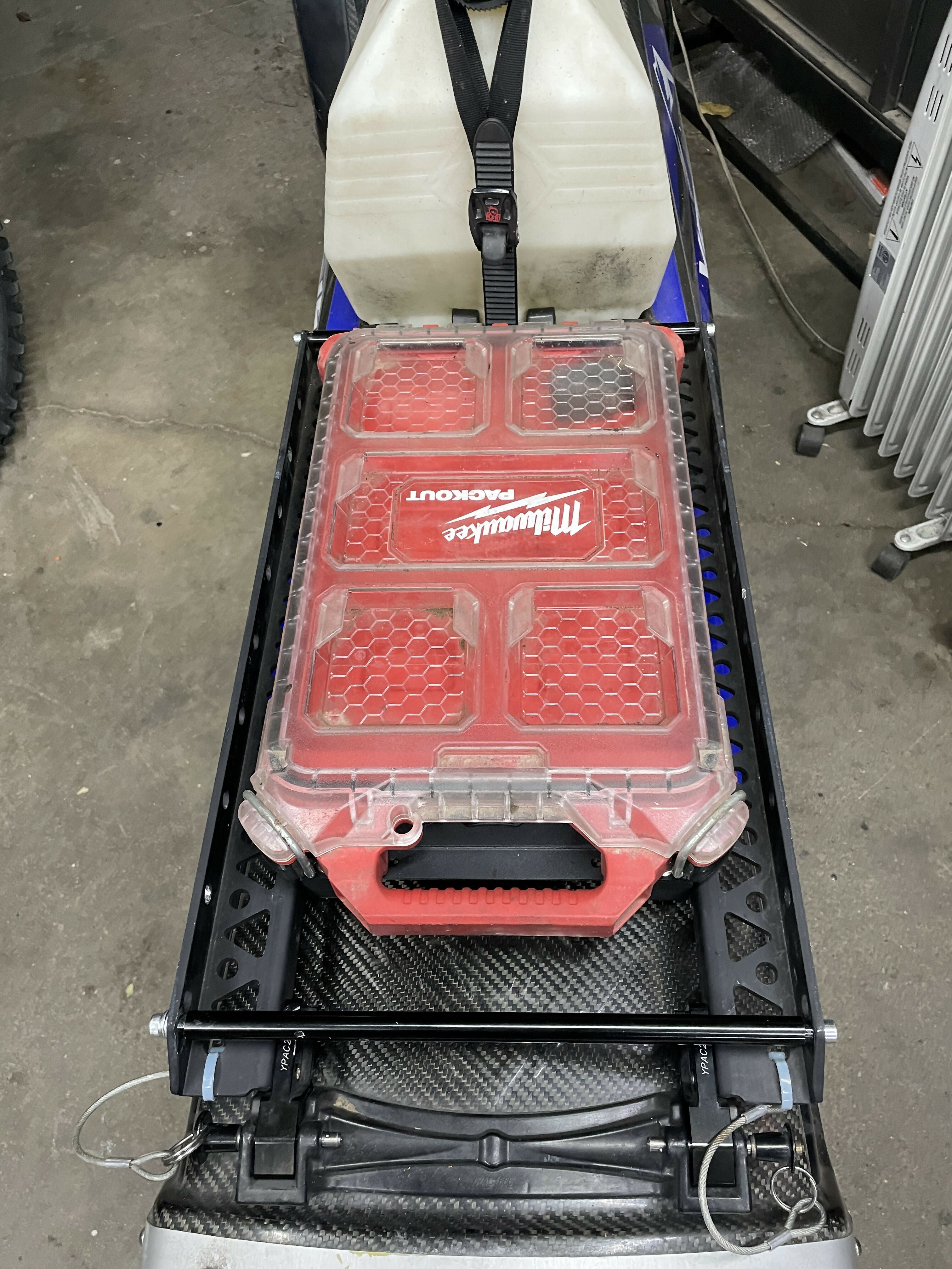 Red Milwaukee tool box on a cart with a white container above it in an indoor setting.