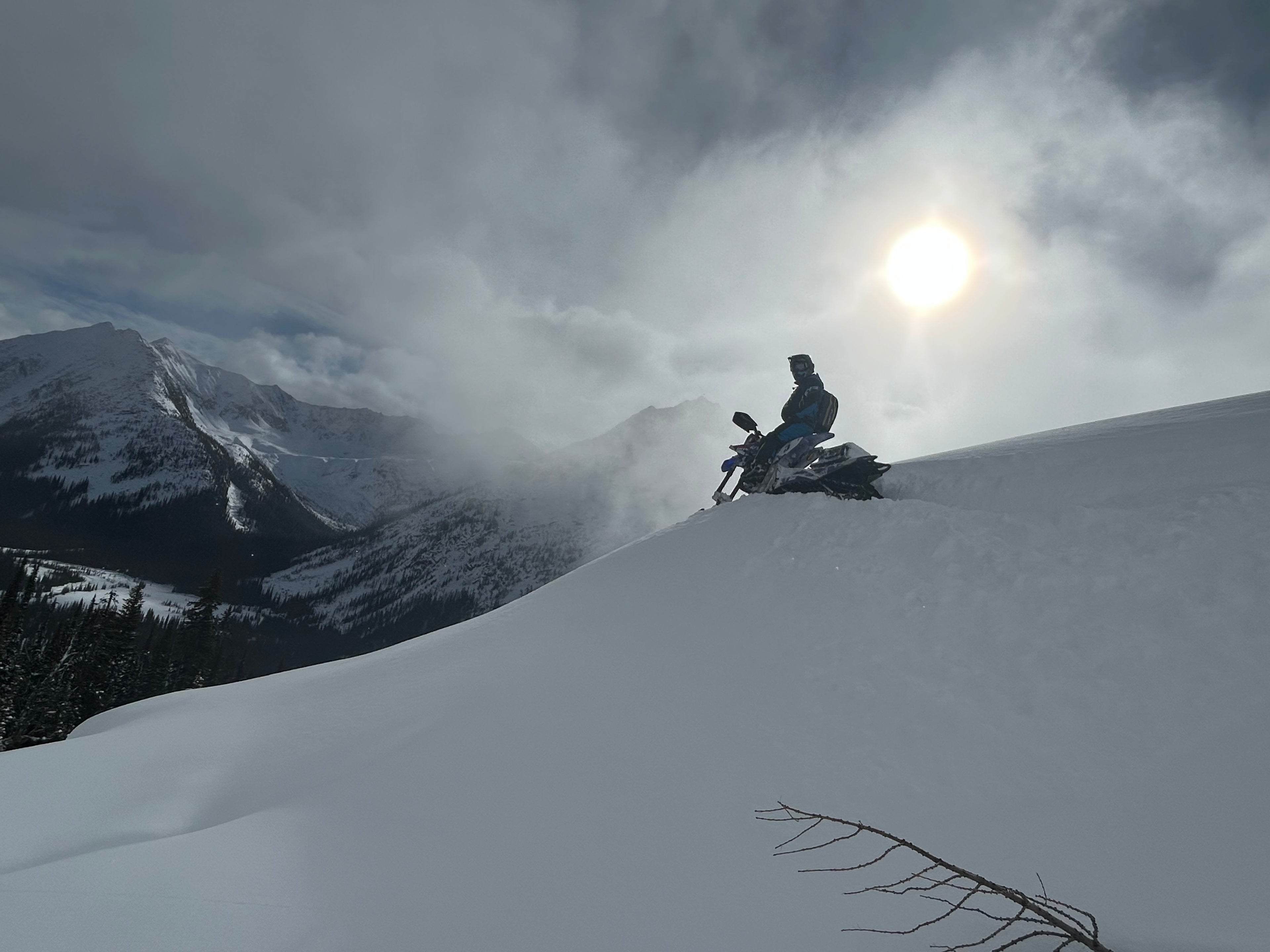 one man on a snowbike in a snowy mountain landscape with a bright sun in the background.