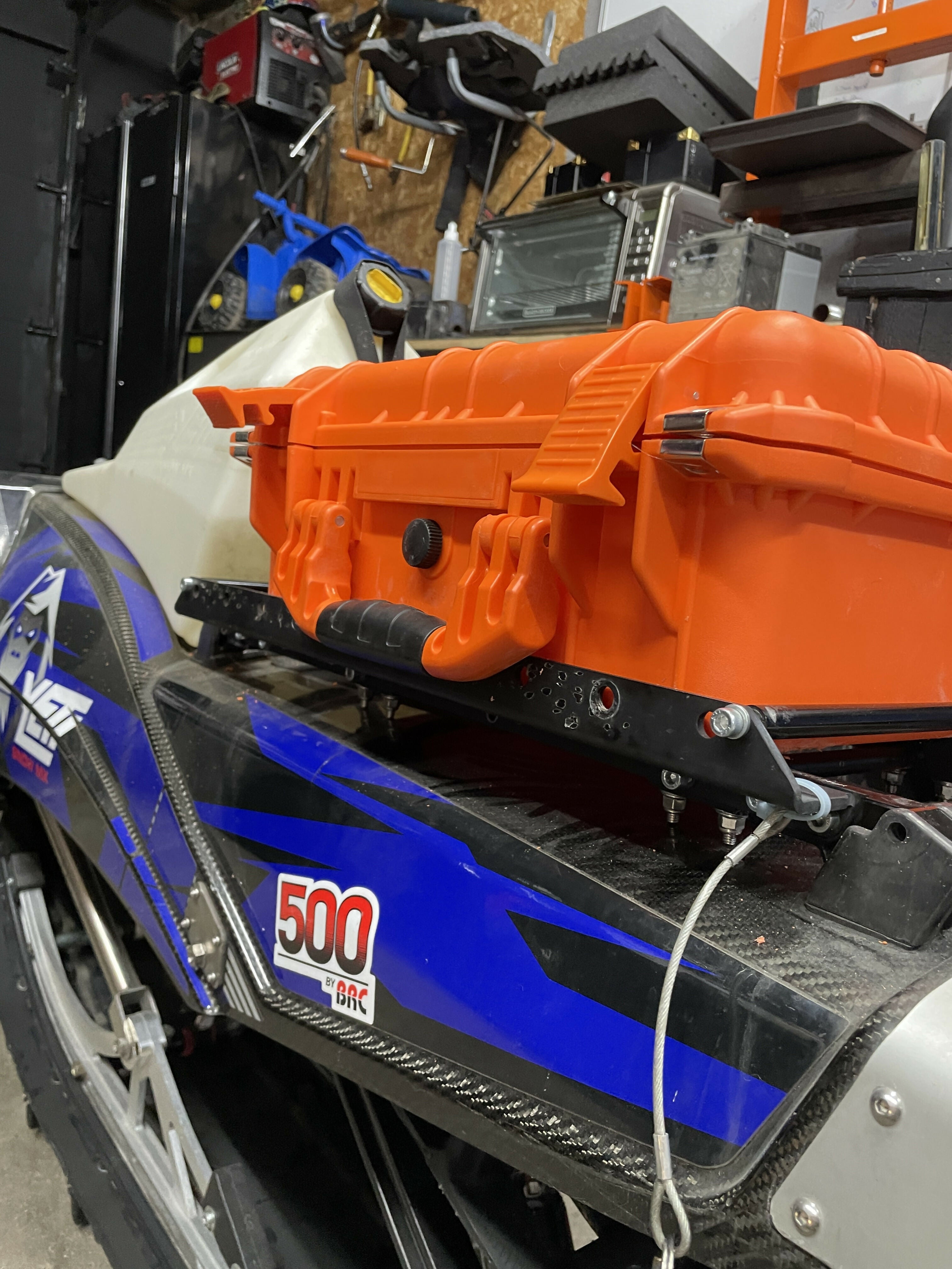 Blue and orange snowmobile with a visible model number in a workshop setting