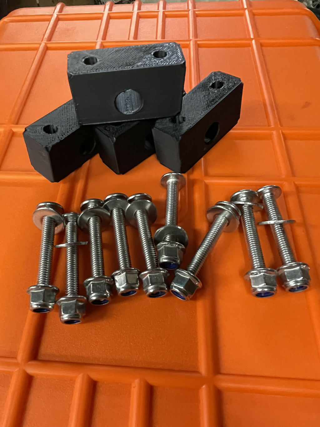 Black metal brackets and screws on an orange surface