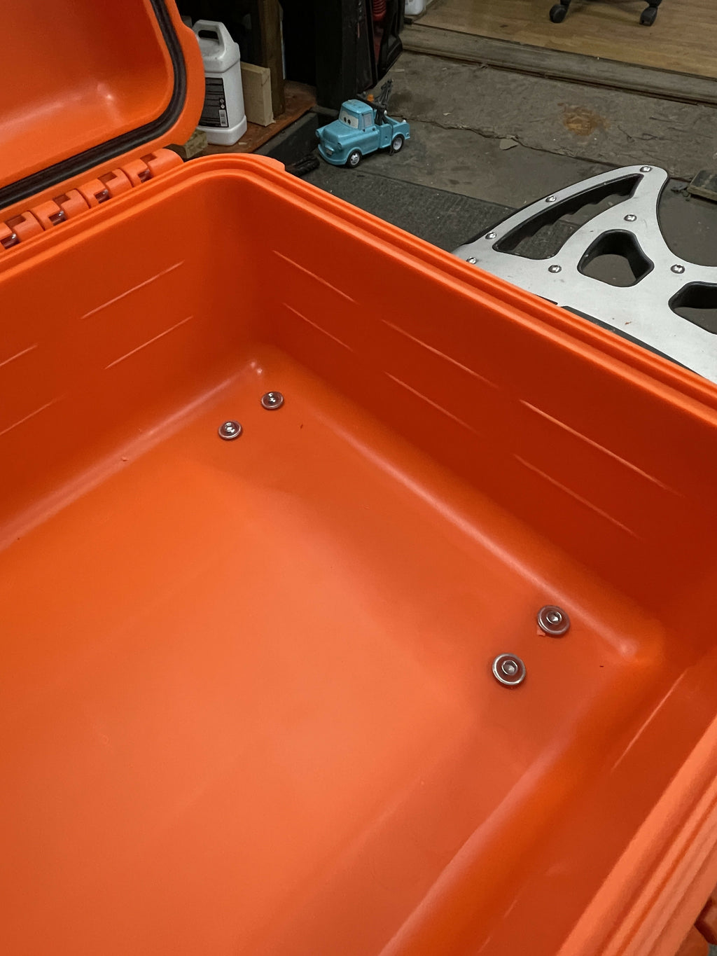 Close-up of an orange toolbox with screws inside, on a workshop floor.